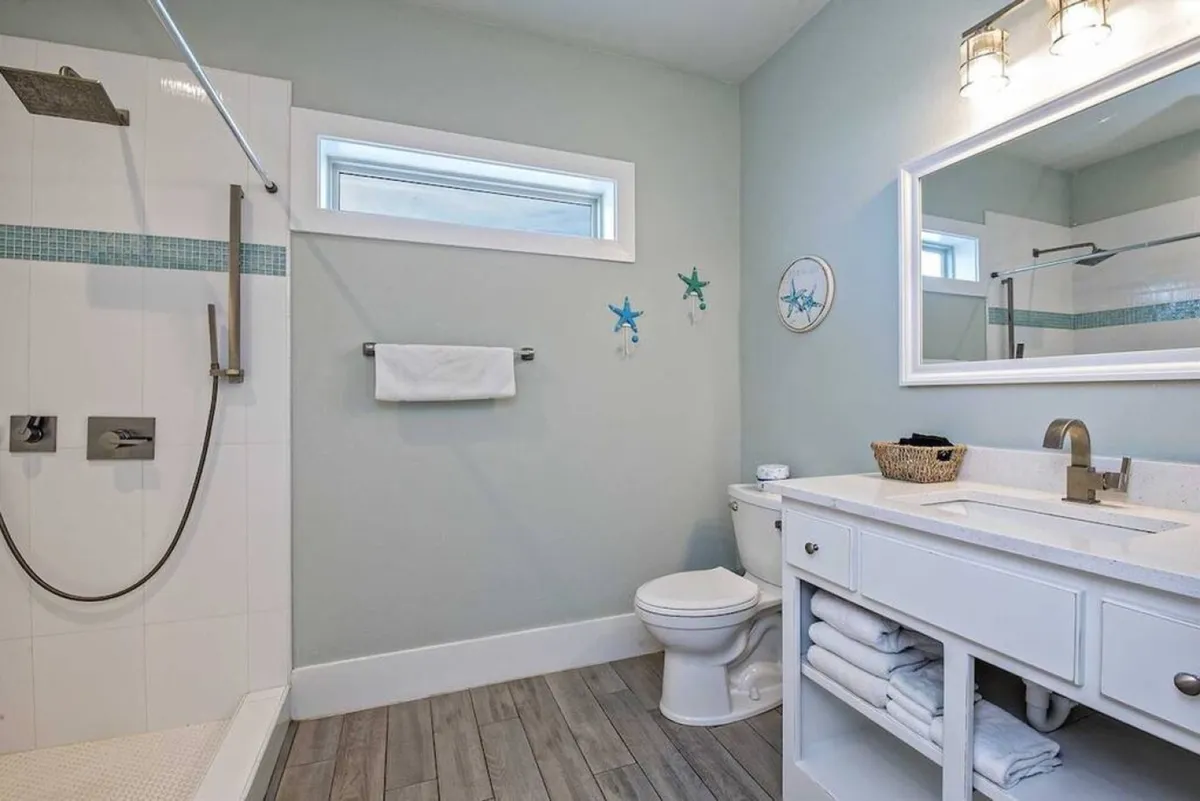 A modern en-suite bathroom featuring a spacious shower area, a vanity with sink, toilet, and tasteful decorative elements. The space feels calm, clean, and inviting—ideal for refreshing after a beach day.