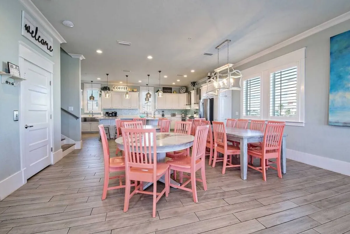 A large dining table set with colorful chairs, adjoining a kitchen area and decorated with vibrant wall art. The space is clearly designed for family gatherings, celebrations, and social meals, offering both functionality and an inviting atmosphere for memorable dining experiences.