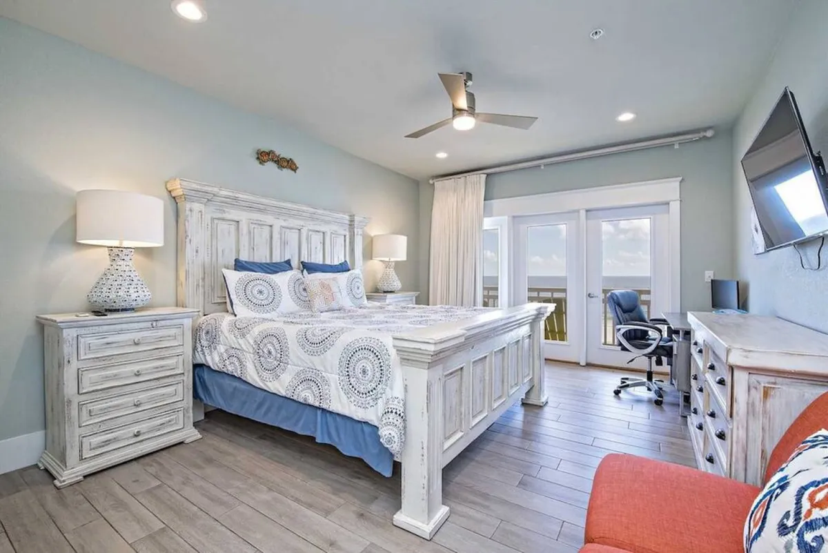 A tranquil bedroom with a large bed, nightstands, sliding glass doors opening to an outdoor space, and a wall-mounted television. The setting feels private and cozy, perfect for relaxing in bed while enjoying natural light and a glimpse of the outdoors.
