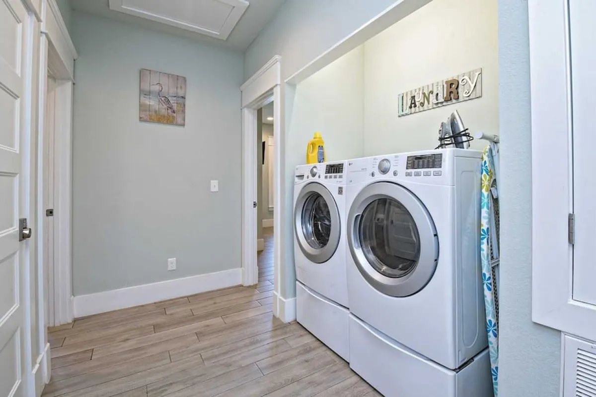 A practical, organized laundry room featuring a front-loading washing machine and dryer, an ironing board, and a decorative laundry sign. The space is clean and inviting, making it suitable for handling large volumes of laundry for families or groups.